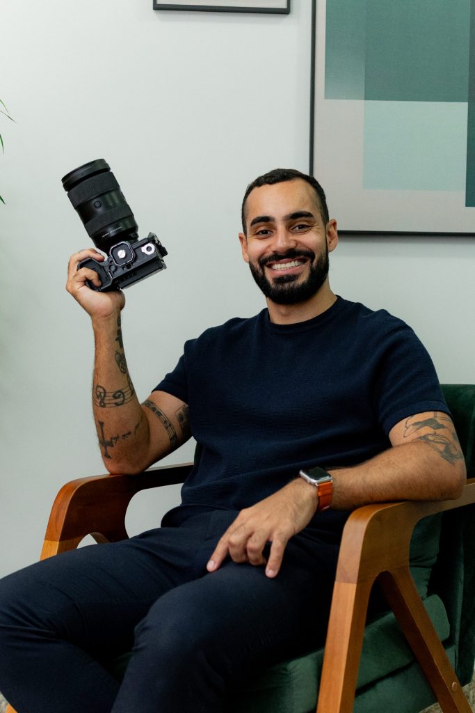 Yuri Fandangos sentado e sorrindo segurando uma câmera.